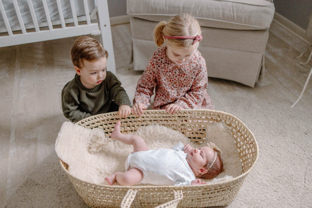 newborn baby in moses basket with siblings overlooking her