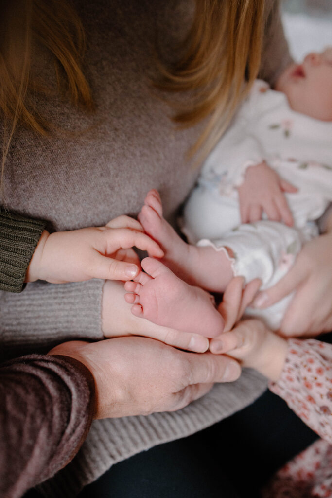 newborn feet with siblings hands tickling